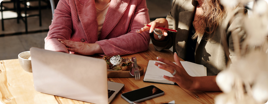 A photo of two people collaborating using a laptop while having lunch in a coffee shop